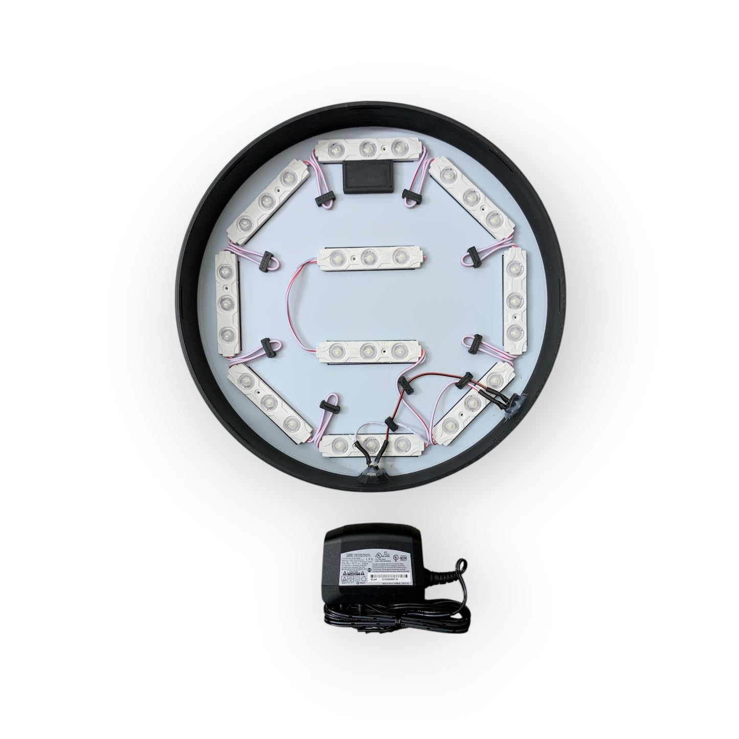 Circular LED light fixture with wiring and a power adapter on a white background